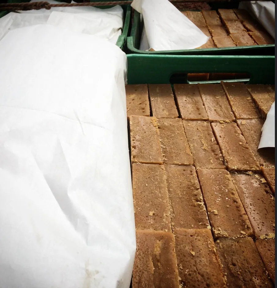 Rectangular blocks of panela arranged in paper-lined green crates.